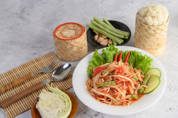 Ensalada de papaya tailandesa en un plato blanco con arroz pegajoso