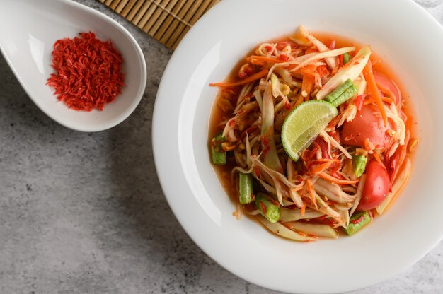 Ensalada de papaya tailandesa en un plato blanco y camarones secos