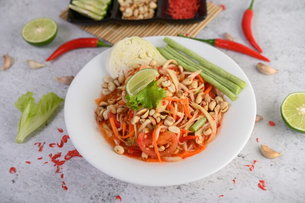 Ensalada de papaya tailandesa en un plato blanco con chile, limón y ajo.