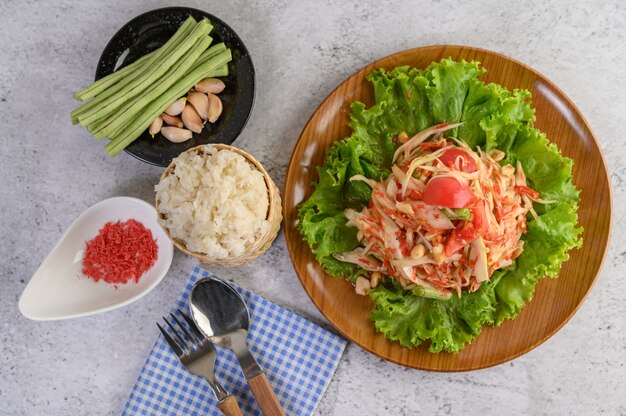 Ensalada de papaya tailandesa en un plato de madera con arroz pegajoso