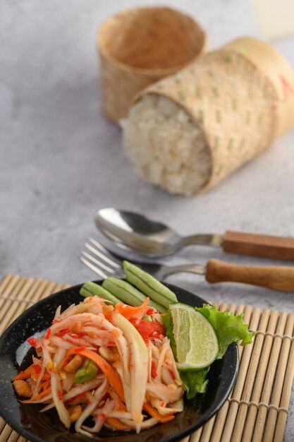 Ensalada de papaya tailandesa en un plato negro con arroz pegajoso