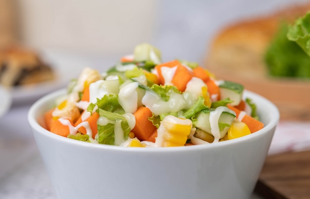 Ensalada de pepino, maíz, zanahoria y lechuga en una taza blanca.