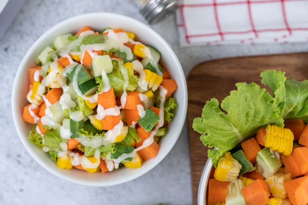 Ensalada de pepino, maíz, zanahoria y lechuga en una taza blanca.