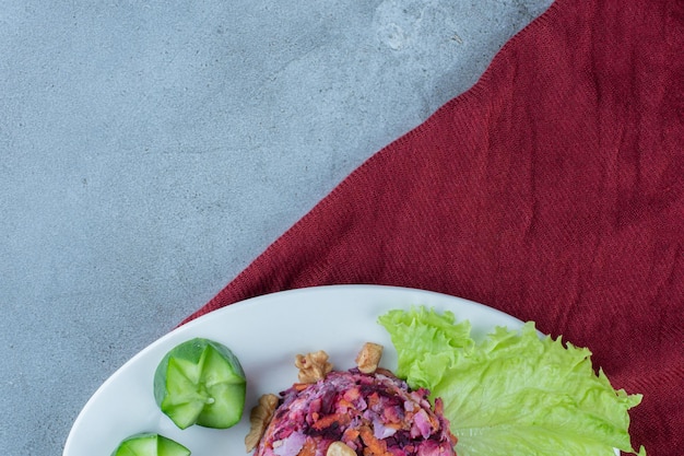 Ensalada pequeña de remolacha, zanahoria y coliflor. adornado con nueces, pepinos y hojas de lechuga en la superficie de mármol