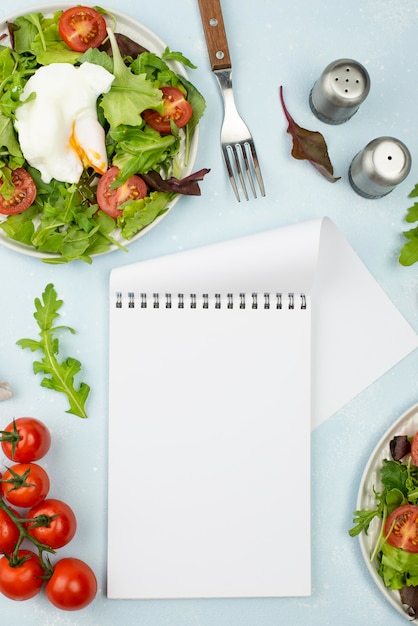 Ensalada plana con huevo frito y tomates con bloc de notas en blanco