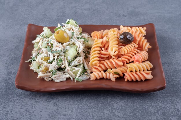 Ensalada de pollo y pasta fusilli en placa marrón.