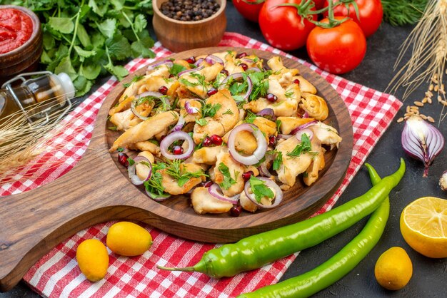 Ensalada de pollo vista frontal con verduras frescas sobre una superficie oscura