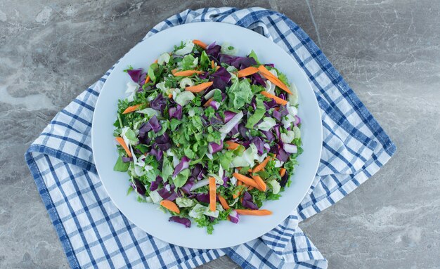 Ensalada preparada con verduras frescas, en plato, sobre la toalla, sobre la mesa de mármol.