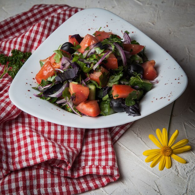 Ensalada de primer plano con tomate, pepino, lechuga, cebolla, aceitunas en un mantel de plato blanco