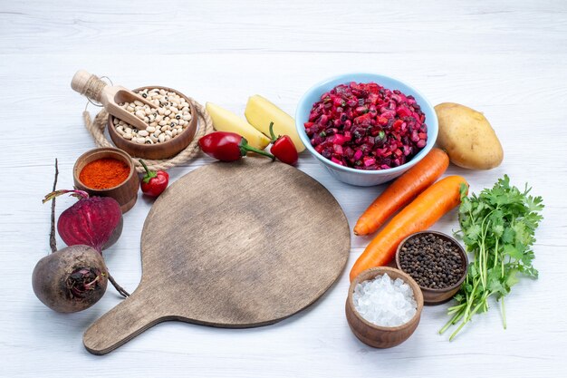 Ensalada de remolacha fresca con verduras frescas en rodajas junto con frijoles crudos, zanahorias, patatas en un escritorio de luz