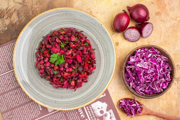 Ensalada de remolacha saludable vista superior en una placa gris con cebollas rojas y repollo picado en un recipiente sobre una mesa de madera