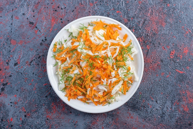 Foto gratuita ensalada de repollo blanco y zanahoria en un plato sobre la mesa negra.