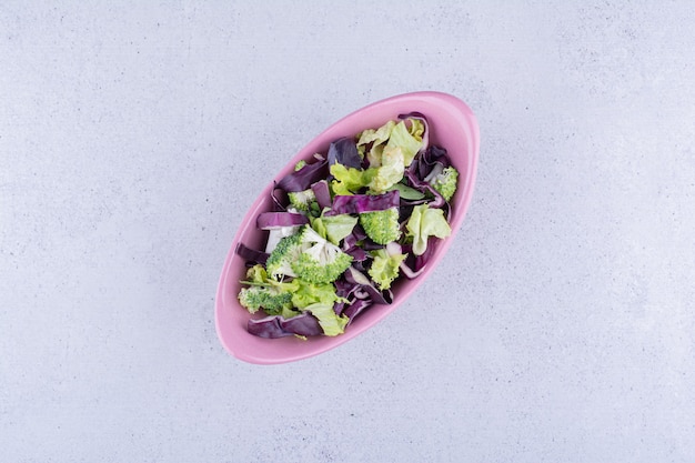 Ensalada de repollo rojo y brócoli en un recipiente ovalado sobre fondo de mármol. Foto de alta calidad