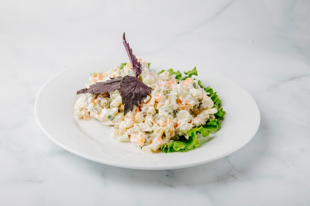 Ensalada rusa del stolichni con basilic rojo y lechuga en una placa blanca en un fondo blanco.