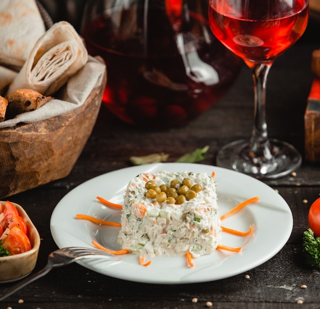 Ensalada rusa stolichni con vino tinto y pan.