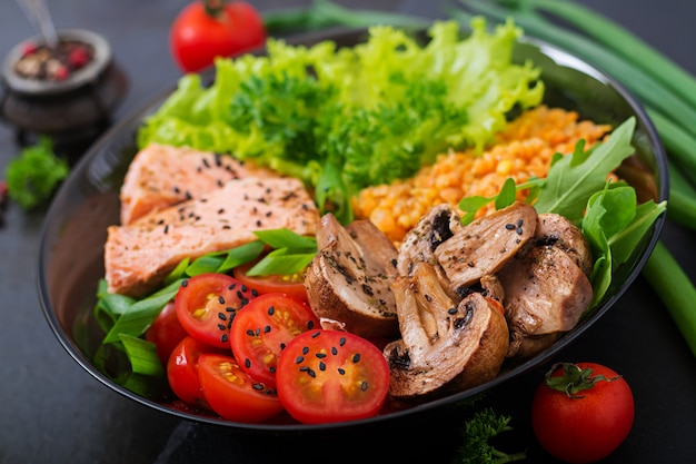 Ensalada saludable con salmón, tomate, champiñones, lechuga y lentejas en la oscuridad