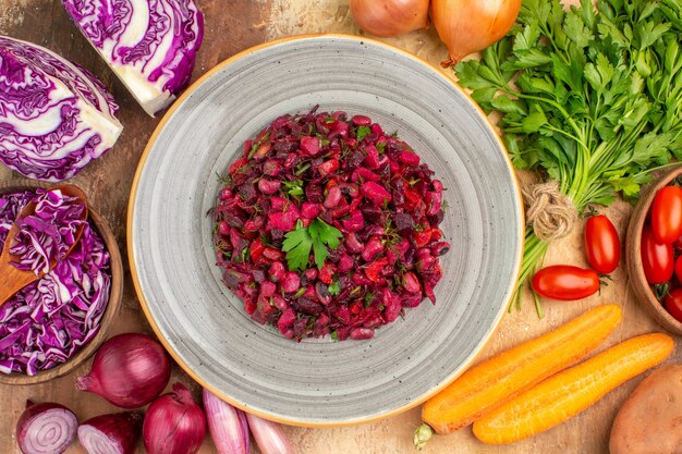 Ensalada saludable de vista superior en un plato de cerámica con verduras frescas cerca, como un tazón de col roja y perejil con tomates roma, zanahoria, patatas y cebollas en una mesa de madera