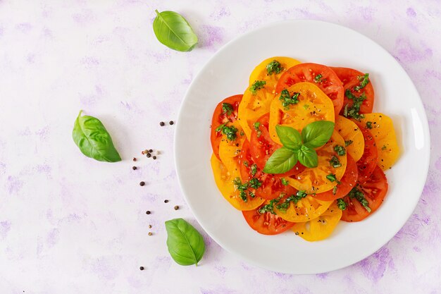 Ensalada de tomate amarillo y rojo con pesto de albahaca sobre una mesa de luz. Endecha plana. Vista superior