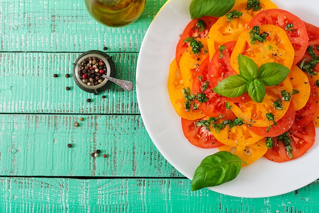 Ensalada de tomate amarillo y rojo con pesto de albahaca sobre una mesa de luz. Endecha plana. Vista superior