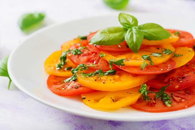 Ensalada de tomate amarillo y rojo con pesto de albahaca sobre una mesa de luz.