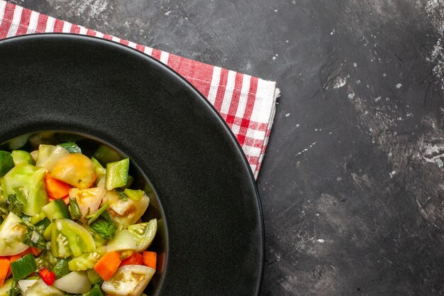 Ensalada de tomate verde de la mitad superior vista en placa ovalada en servilleta sobre fondo oscuro