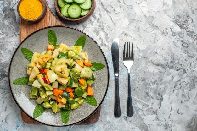 Ensalada de tomate verde de vista superior cercana en placa ovalada en tenedor y cuchillo de tabla de cortar sobre fondo oscuro