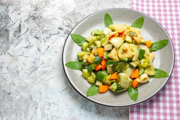 Ensalada de tomate verde de vista superior en mantel rosa placa ovalada sobre superficie gris