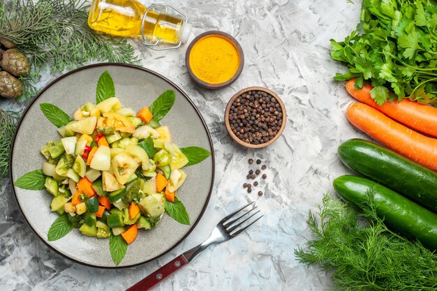 Ensalada de tomate verde de vista superior en placa ovalada un tenedor especias botella de aceite verduras sobre fondo oscuro