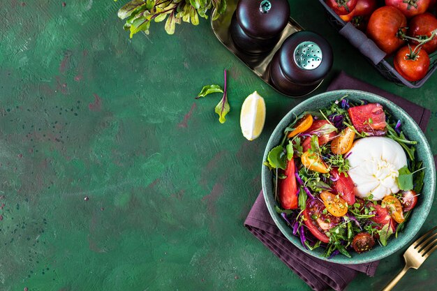 Ensalada con tomates, rúcula, queso burrata y microvegetales sobre un fondo de piedra verde, vista superior, espacio de copia