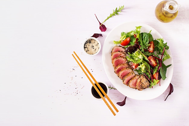 Ensalada tradicional japonesa con trozos de atún ahi a la parrilla medio raro y sésamo con ensalada de vegetales frescos en un plato.
