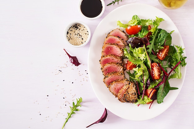 Ensalada tradicional japonesa con trozos de atún ahi a la parrilla medio raro y sésamo con ensalada de vegetales frescos en un plato.