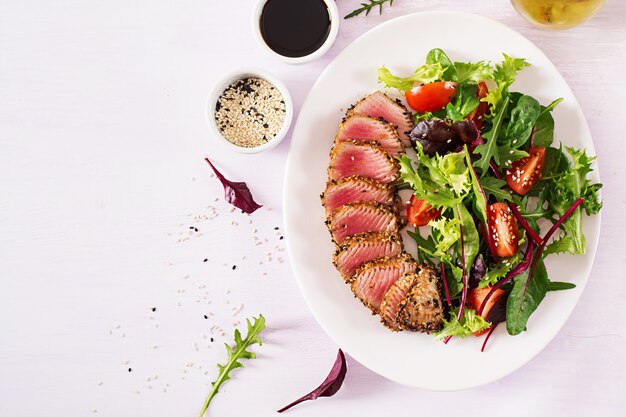 Ensalada tradicional japonesa con trozos de atún ahi a la parrilla medio raro y sésamo con ensalada de vegetales frescos en un plato.