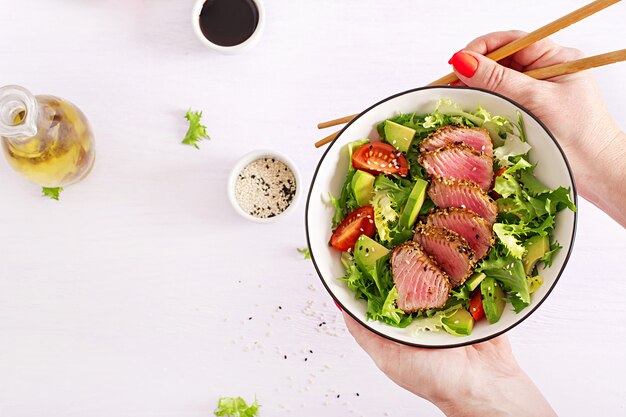 Ensalada tradicional japonesa con trozos de atún ahi a la parrilla medio raro y sésamo con ensalada de vegetales frescos en un plato.