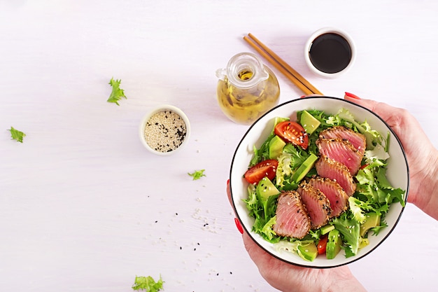 Ensalada tradicional japonesa con trozos de atún ahi a la parrilla medio raro y sésamo con ensalada de vegetales frescos en un plato.