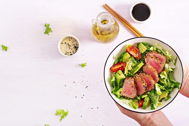 Ensalada tradicional japonesa con trozos de atún ahi a la parrilla medio raro y sésamo con ensalada de vegetales frescos en un plato.