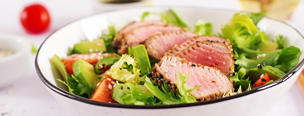 Ensalada tradicional japonesa con trozos de atún ahi a la parrilla medio raro y sésamo con vegetales frescos en un tazón.