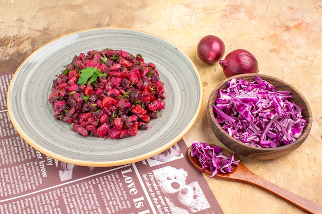 Ensalada vegana de vista superior con hojas verdes y verduras en un plato de color gris con un tazón de col picada y cebollas en la luz de una mesa de madera