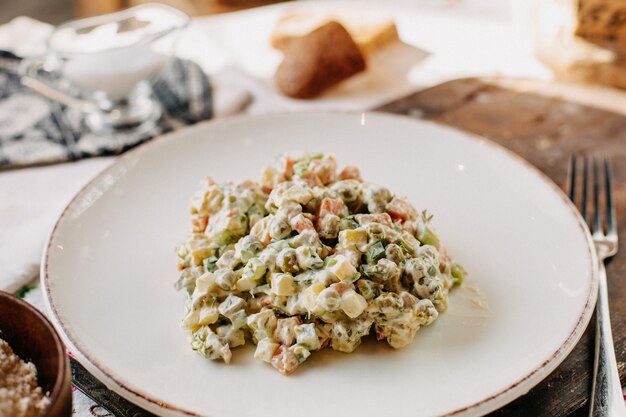 ensalada de vegetales mayyonaise salado sabroso dentro de un plato blanco junto con un tenedor de panes durante el día