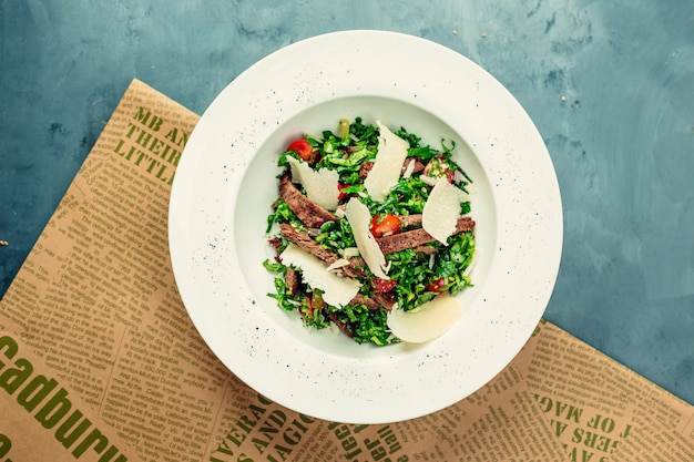 Ensalada verde con carne y queso picado dentro de un tazón blanco.