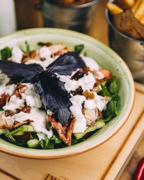 Ensalada verde con cubitos de queso blanco, galletas saladas y hojas basílicas rojas dentro del tazón verde