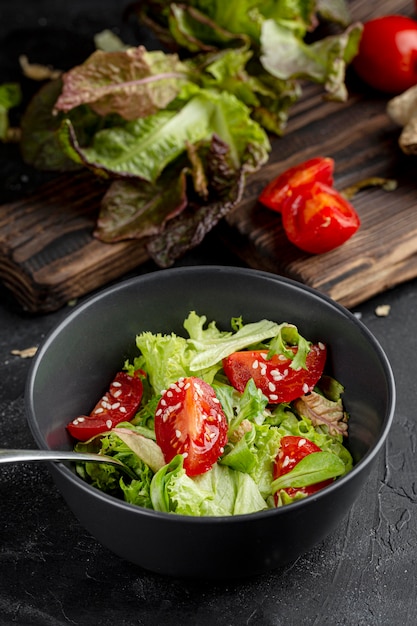 Ensalada verde fresca de alto ángulo con tomates en un recipiente oscuro