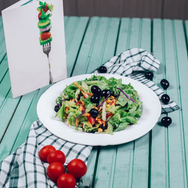 Ensalada verde con hierbas, aceitunas negras y tomate.