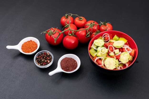 Ensalada verde con tomate y verduras frescas aisladas en superficie negra