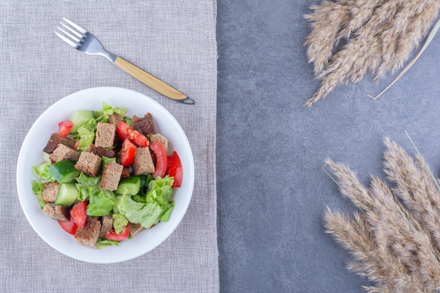 Ensalada de verduras con corteza seca sobre un mantel junto a tallos de pasto seco en la superficie de mármol