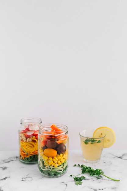 Ensalada de verduras en dos tarros de masón con un vaso de jugo de limón en la parte superior de mármol