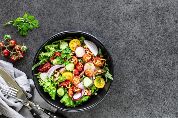 Ensalada de verduras frescas en un plato sobre un fondo negro. Vista superior