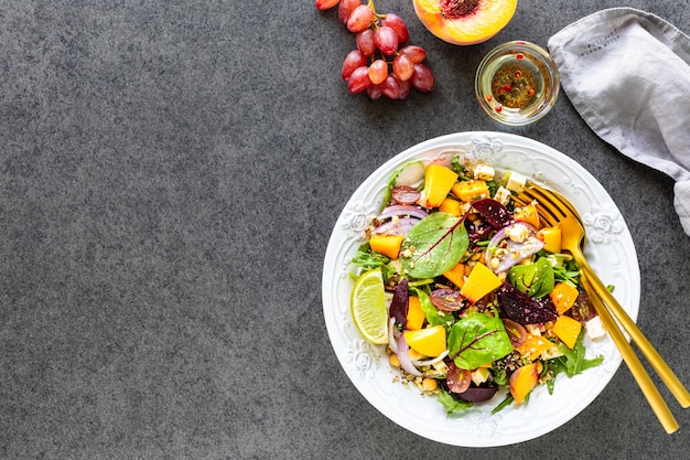 Ensalada de verduras frescas con remolacha, rúcula, cebolla morada, acedera, garbanzos, melocotón y uvas en un plato blanco