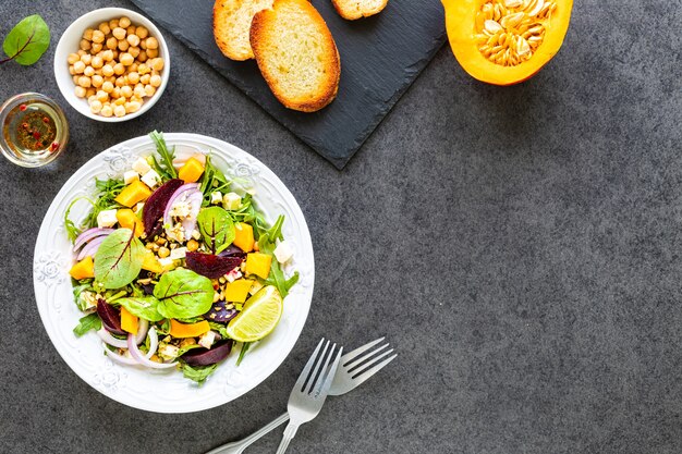 Ensalada de verduras frescas con remolacha, rúcula, cebolla morada y acedera en un plato blanco con calabaza, tostadas y garbanzos