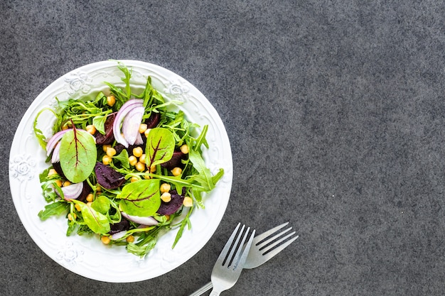 Ensalada de verduras frescas con remolacha, rúcula, cebolla roja y acedera en una placa blanca.