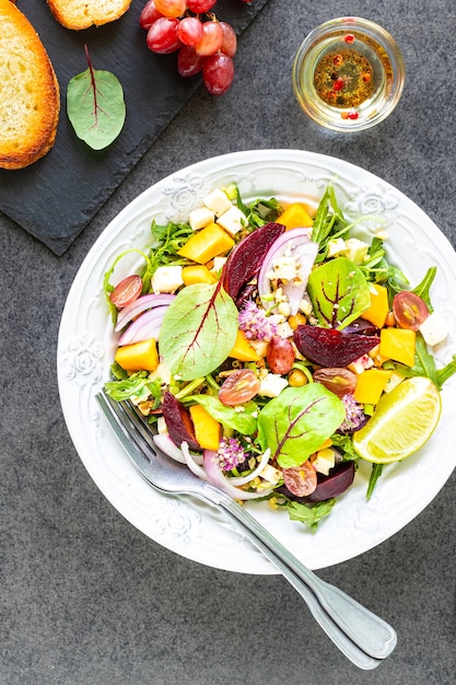 Ensalada de verduras frescas con remolacha, rúcula, cebolla roja y acedera en un plato blanco con calabaza y uvas